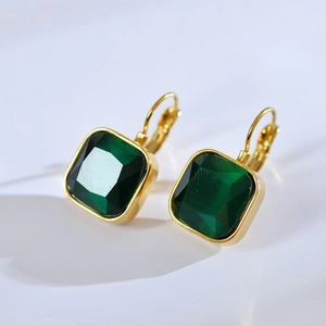Detailed close-up of gold hook earrings featuring square-cut emerald green gemstones