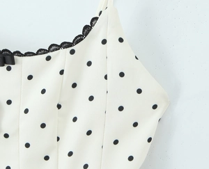 Detail of white polka dot dress featuring delicate black lace trim and small ribbon bow