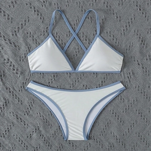 Flat lay of a white bikini set with sky blue trim on textured gray fabric background