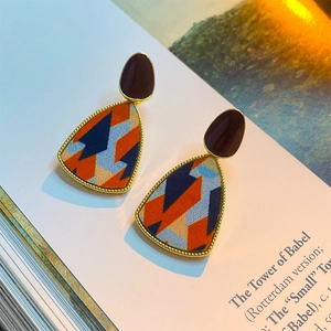 Macro detail of geometric fabric triangle earrings with gold edges on an open book