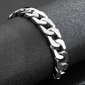 Macro shot of silver Cuban link bracelet on black textured pedestal showing polished steel