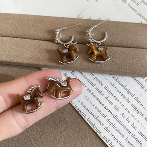 Detail of horse-shaped zircon earrings in amber resin with silver needles on jewelry box
