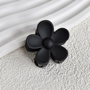 Close-up of matte black flower hair claw clip on a minimalist white stone background