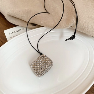 Detailed macro shot of silver hollow woven grid pendant on black wax rope necklace