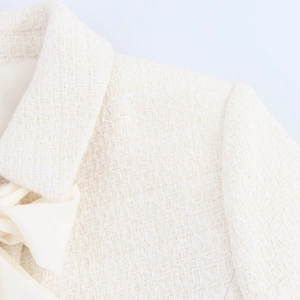 Close-up of white tweed jacket featuring texture detail and an elegant bow on the collar