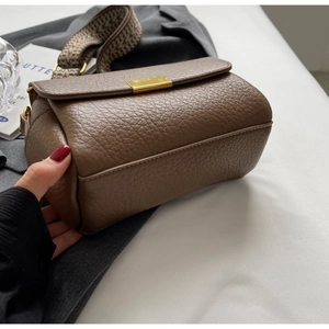 Détail du sac bandoulière en cuir marron foncé avec boucle dorée et large sangle tissée