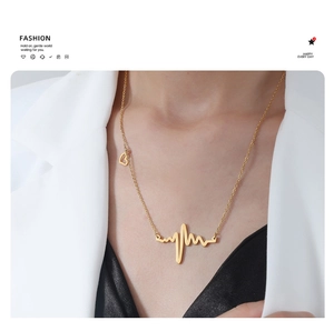 Detail of gold heartbeat necklace with heart charm on female model in white blazer