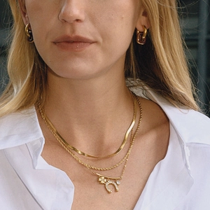 Detailed shot of layered gold necklaces with horseshoe charm and resin hoop earrings