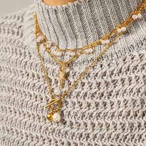 Double-layered gold pearl necklace with star pendant and toggle clasp on a sweater
