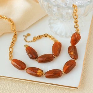 Detail of amber resin stone and golden stainless steel chain jewelry set on plate