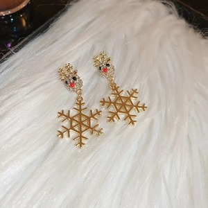 Detail of Christmas snowflake and reindeer stud earrings on white plush fabric