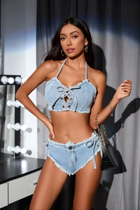 Dettaglio del top all'americana in denim azzurro con lacci e pantaloncini con frange