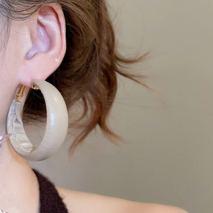 Close-up of large beige leather hoop earrings with gold accents on model ear