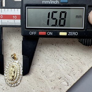 Digital caliper measuring the 15.8 mm width of a gold Virgin Mary zircon pendant
