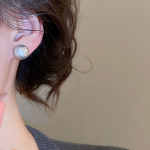 Close-up of a large grey pearl stud earring worn on ear with elegant metallic luster