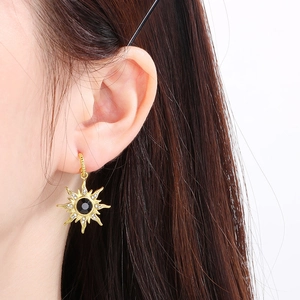 Gros plan d'une boucle d'oreille soleil dorée avec gemme noire et cristaux brillants