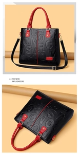 Detail of black embossed leather handbag with red contrast strap and gold hardware