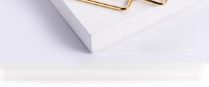 Detail of polished gold square hoop earring on a textured white stone pedestal base