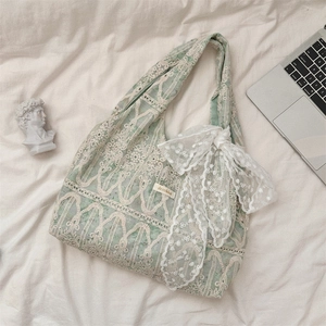 Detail of light green lace tote bag featuring floral texture and large white bow decoration