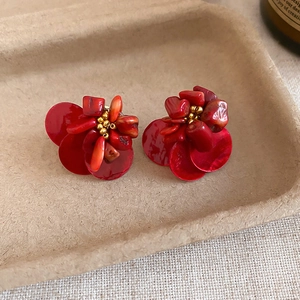 Detailed view of red floral stud earrings with shell petals and beaded centerpiece