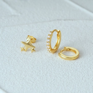 Three-piece gold earring set with star stud and crystal-encrusted hoop on stone surface