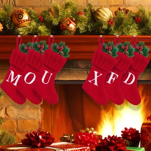 Detail of red knit Christmas stockings with white letters and festive pine cone accents