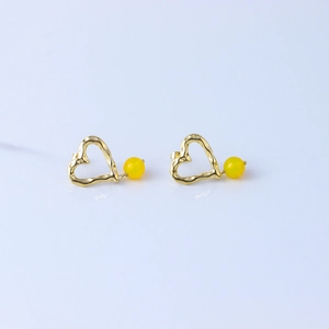 Detailed macro view of an irregular golden heart earring with bright yellow bead accent