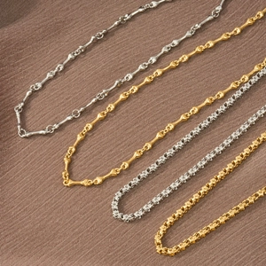 Dettaglio di collane in acciaio al titanio oro e argento con maglie a fiore e osso