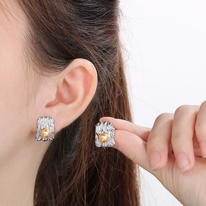 Detailed close-up of irregular textured silver earrings with a round gold pearl inlay