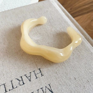 Detailed close-up of a cream acrylic irregular wave open bangle on a rustic book cover
