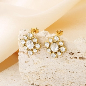Macro shot of gold flower stud earrings with diamonds and central oval crystal