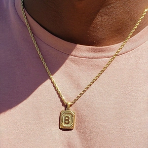 Detail shot of a golden twist chain necklace with a textured rectangular B letter pendant