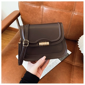 Détail du sac selle en cuir marron avec rabat festonné et fermoir métallique doré