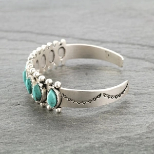 Bohemian silver open cuff bracelet with five turquoise stones on a dark stone surface