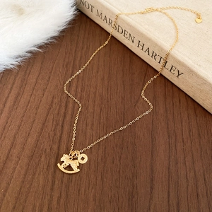 Detail of gold plated necklace with rocking horse and coin pendants on wood surface