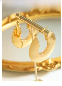 Detailed view of glossy gold-plated U-shaped earrings on a commercial display stand