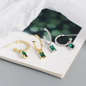 Close-up of gold and silver S925 sterling silver huggie earrings with emerald zircon charms