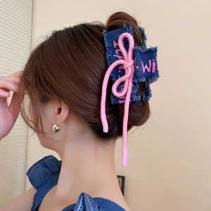 Detail of blue denim hair claw clip featuring pink ribbon bow and frayed edge texture