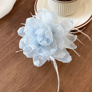 Detail einer hellblauen Organza-Haarklammer mit weißen Federn auf Holzoberfläche
