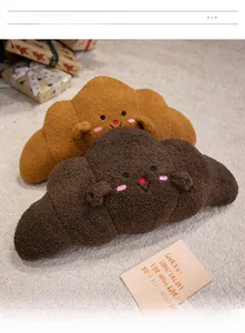 Detail of soft plush croissant pillow with cute embroidered faces on beige carpet