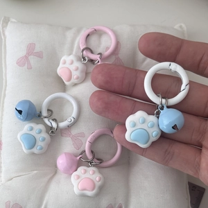 Close-up of cute cat paw keychains with colorful bells and rings on a pink cushion
