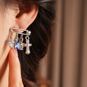 Detailed view of silver safety pin earrings with zircon heart and cross pendants