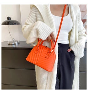 Detail of orange quilted leather shell bag worn as a crossbody purse by a model