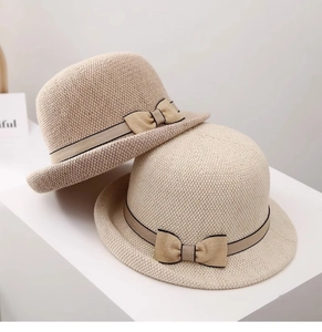 Dettaglio di un cappello di paglia beige chiaro con trama fine e nastro a fiocco con bordo nero