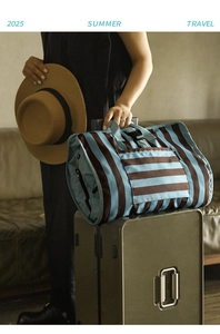 Travel organizer bag with stripes attached to a suitcase handle for easy transport