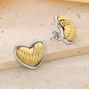 Macro shot of two-tone 18K gold plated heart earrings on beige stone texture