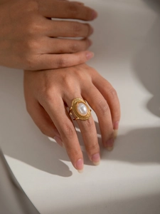 Macro shot of gold vintage ring with oval pearl and woven metal texture on finger