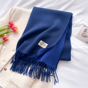 Detail of blue pashmina scarf with fringe and logo tag on white plush jacket