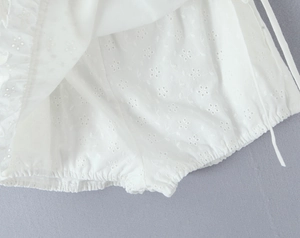 Detailed view of white cotton fabric featuring intricate floral eyelet embroidery and pleats