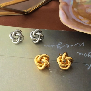 Macro detail of knot-shaped earrings in gold and silver finish on a pearl tray